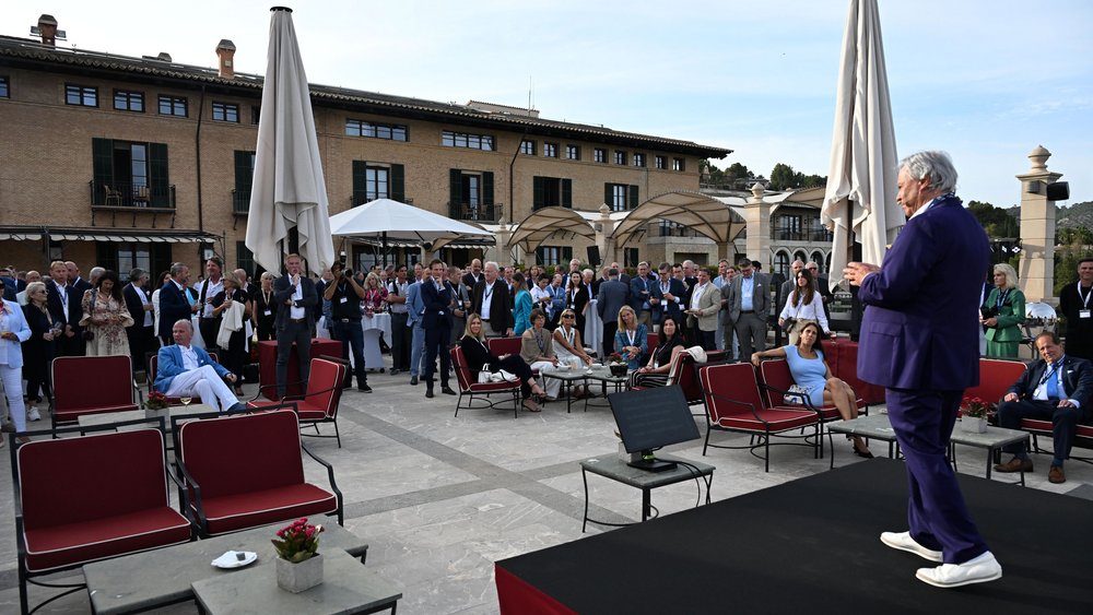 Willi Plattes spricht, umgeben von zuhörenden Teilnehmern und Referenten.